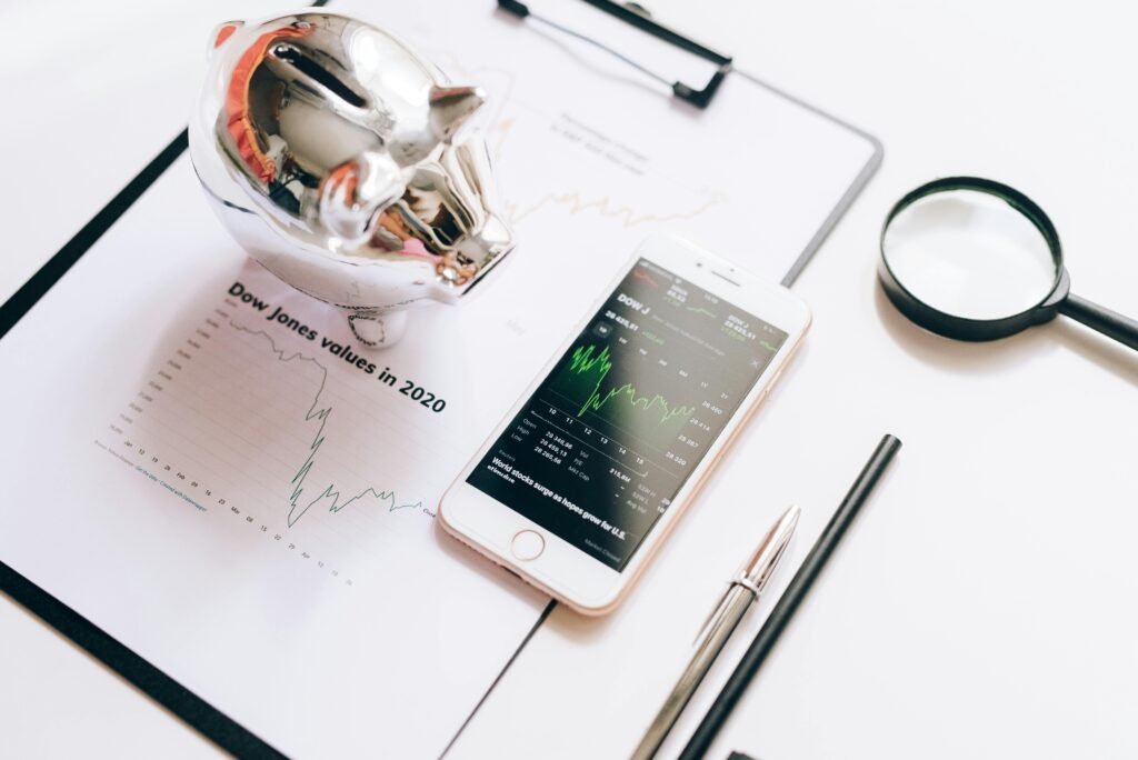 pexels-photo-5562085-5562085 Flat lay of financial tools: chart, smartphone, magnifying glass, and piggy bank.